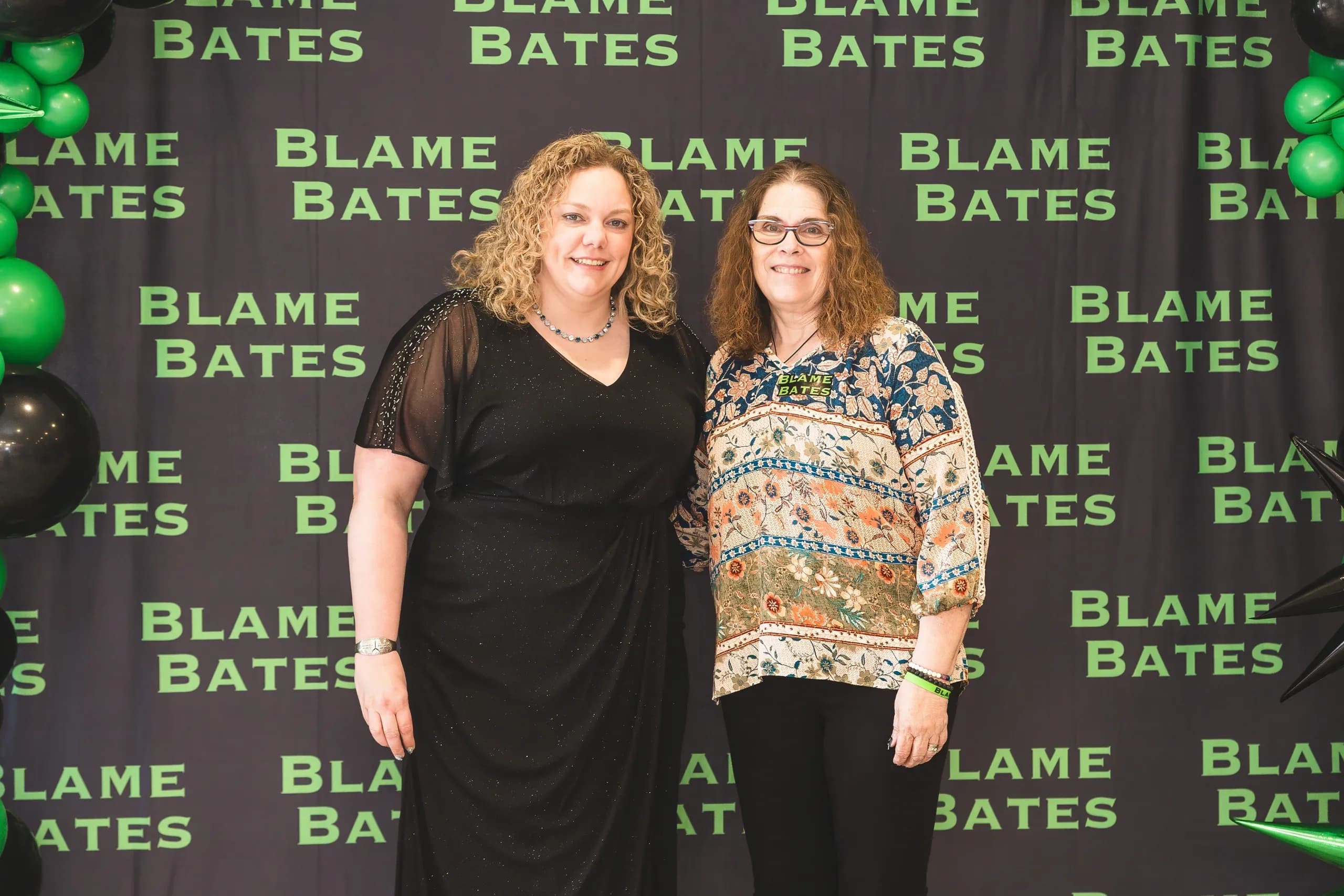 Two guests in front of the Blame Bates balloon wall at the gala.
