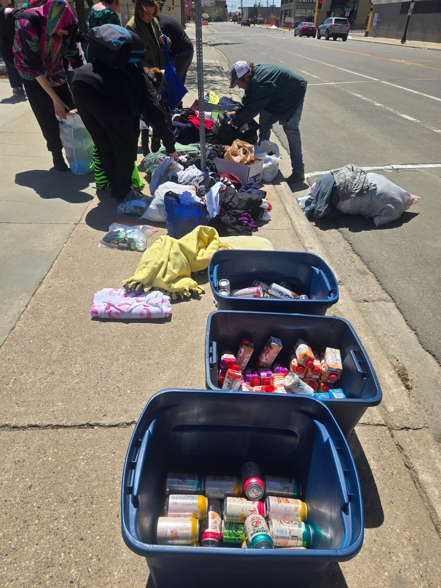 Volunteers sorting donated clothing and bins of canned food on a downtown Fargo sidewalk.